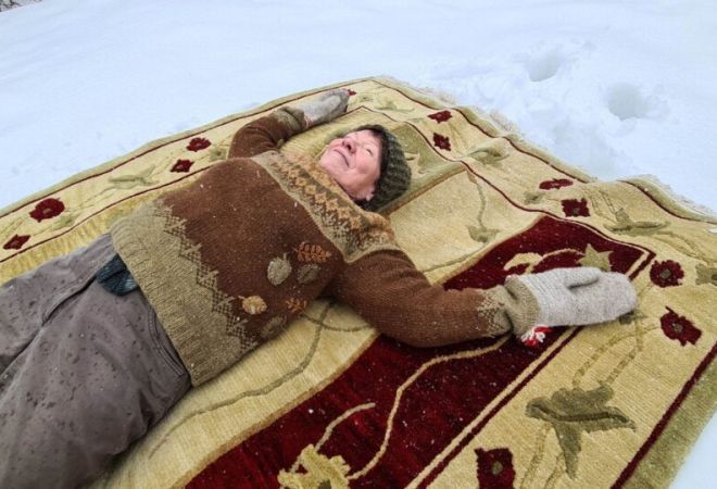 Nainen makaa maton päälle lumessa.