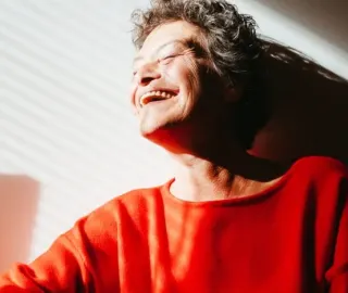 Punapaitainen vanhempi nainen nauraa auringossa.