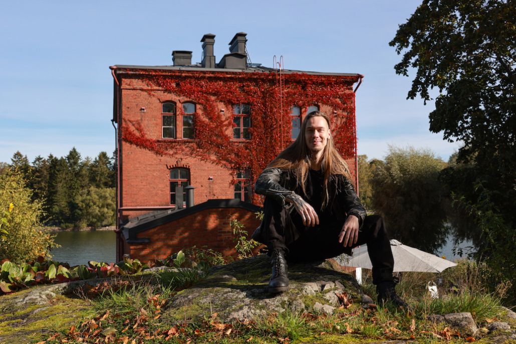 Tiilinen Venetsia-talo ja edustalla pitkähiuksinen istuva, hymyilevä mies.