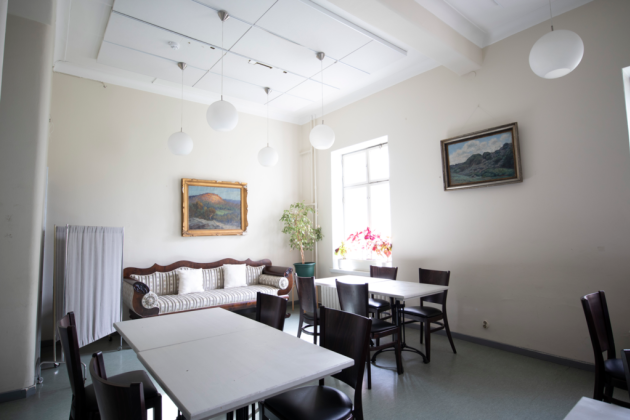 Kuvassa etualalla on pöytiä ja tuoleja. Taka-alalla on sohva, tauluja seinällä ja yksi Osasto5:n ikkunoista.