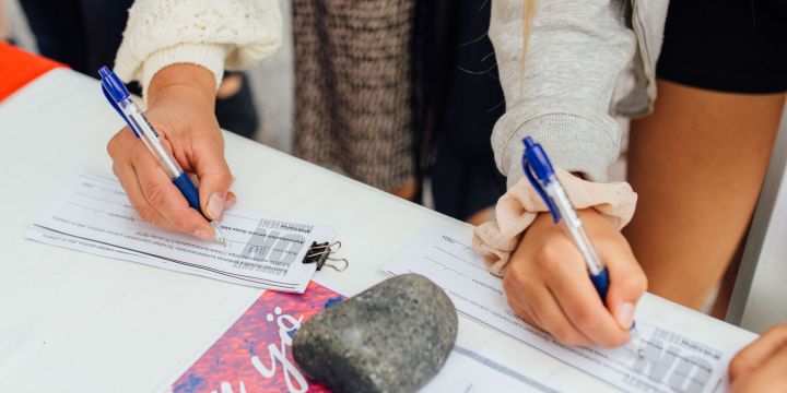 Lähikuva kahden henkilön käsistä allekirjoittamassa kuntalaisaloitelomaketta