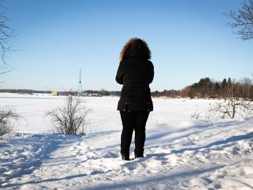 Nainen seisoo lumisessa maisemassa selkä kuvaajaan päin.