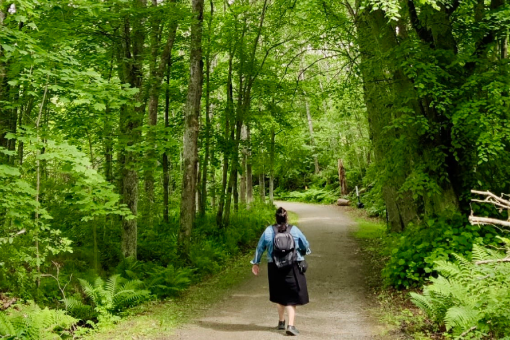Kuvassa nainen kulkee metsän keskellä kulkevaa tietä pitkin.