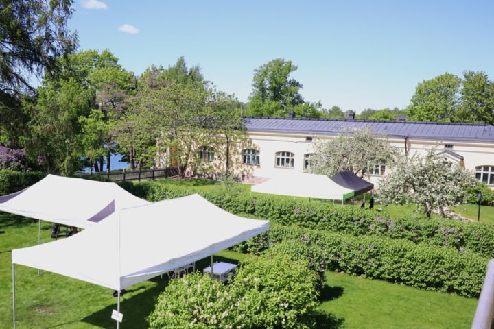 Kuvassa on puutarhapiha päärakennuksen toisen kerroksen parvekkeelta kuvattuna. Etualalla on pensaita ja katoksia ja taka-alalla talon pohjoissiipi.