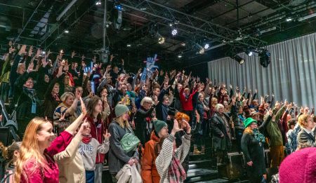 Kuvassa iso sali yleisöä kädet ilmassa kirjasto Oodin salissa.