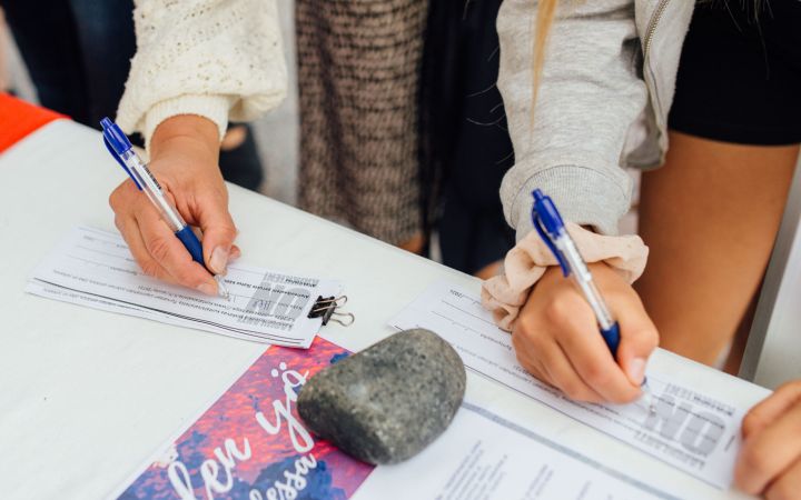 Lähikuva kahden henkilön käsistä allekirjoittamassa kuntalaisaloitelomaketta
