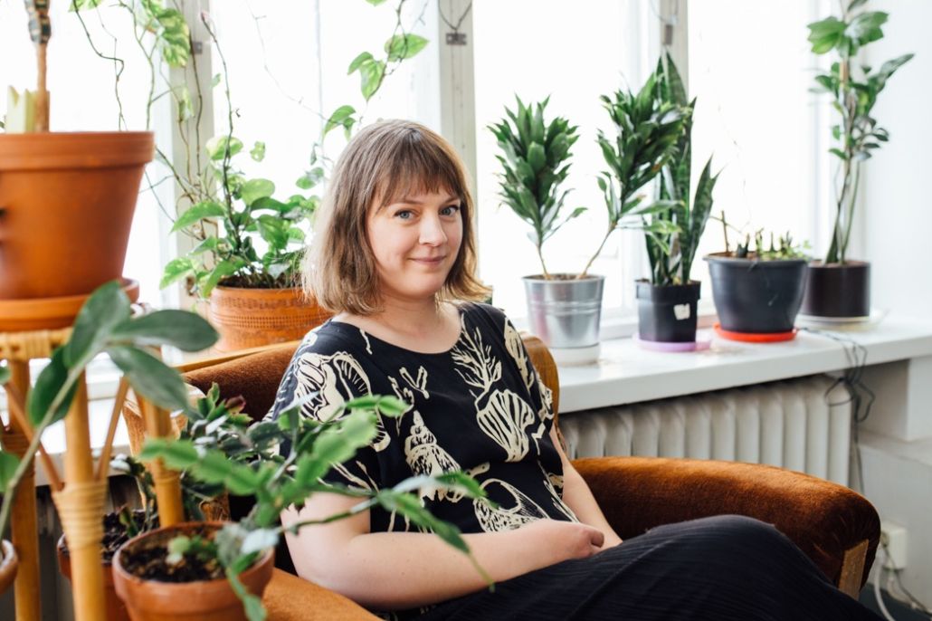 Nainen istuu vanhassa nojatuolissa viherkasvien keskellä.