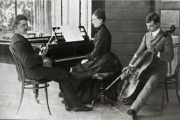 Mustavalkoinen kuva Sibeliuksen sisaruksista. Jean istuu vasemmalla sylissään viulu, Linda keskellä pianon ääressä ja Christian Sibelius oikealla sellon kanssa.