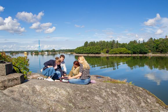 Neljä ihmistä aurinkoisilla Lapinlahden kallioilla meren äärellä keskustelemassa.
