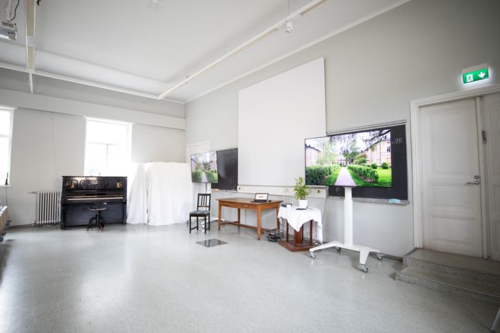 Kuvassa etualalla oikealla on auditorion televisio, keskellä valkokangas ja vasemmalla piano.