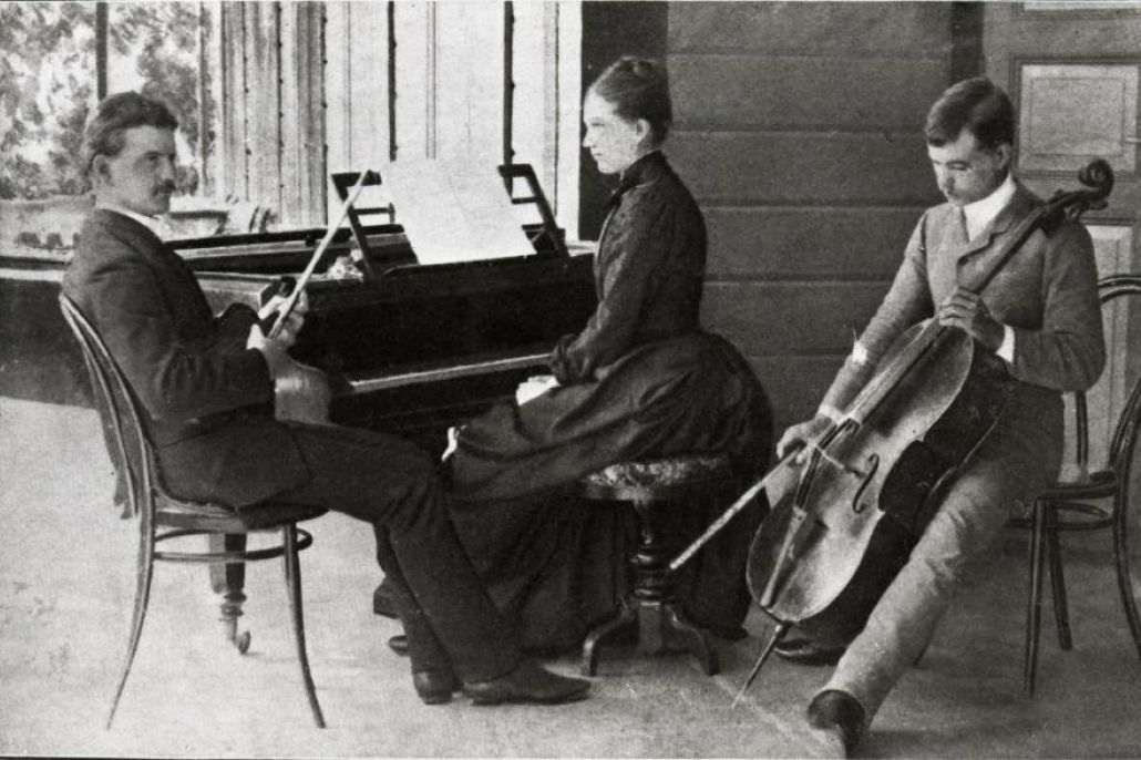 Mustavalkoinen kuva Sibeliuksen sisaruksista. Jean istuu vasemmalla sylissään viulu, Linda keskellä pianon ääressä ja Christian Sibelius oikealla sellon kanssa.