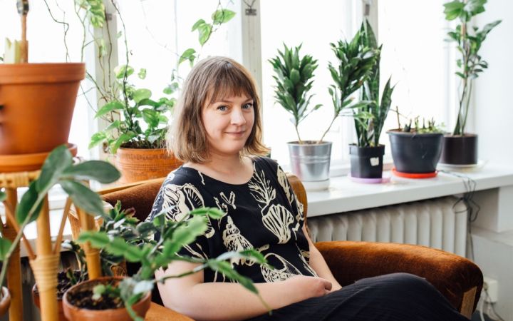 Nainen istuu vanhassa nojatuolissa viherkasvien keskellä.