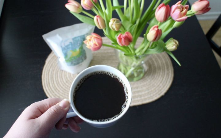 Kuvassa on etualalla kahvikuppi ja takana Save Lapinlahti -kahvipaketti ja tulppaaneja.