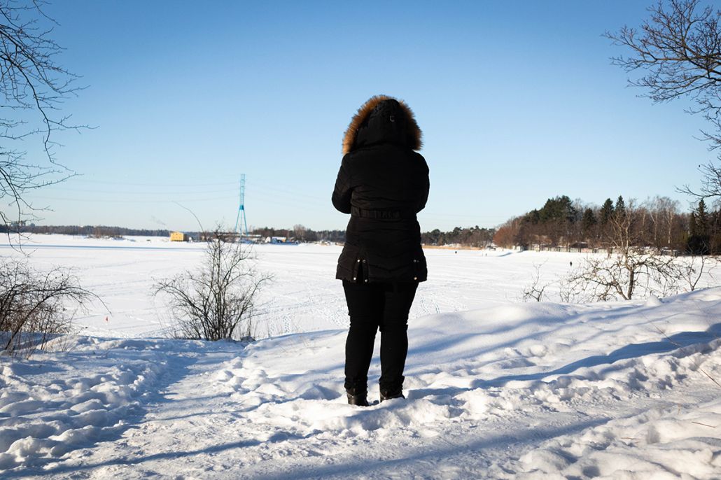 Nainen seisoo lumisessa maisemassa selkä kuvaajaan päin.