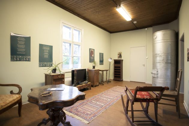 Kuvassa etualalla vasemmalla on pöytä. Taka-alalla on seinän vieressä olevia huonekaluja.