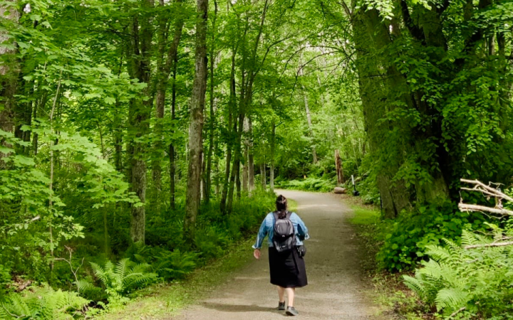 Kuvassa nainen kulkee metsän keskellä kulkevaa tietä pitkin.