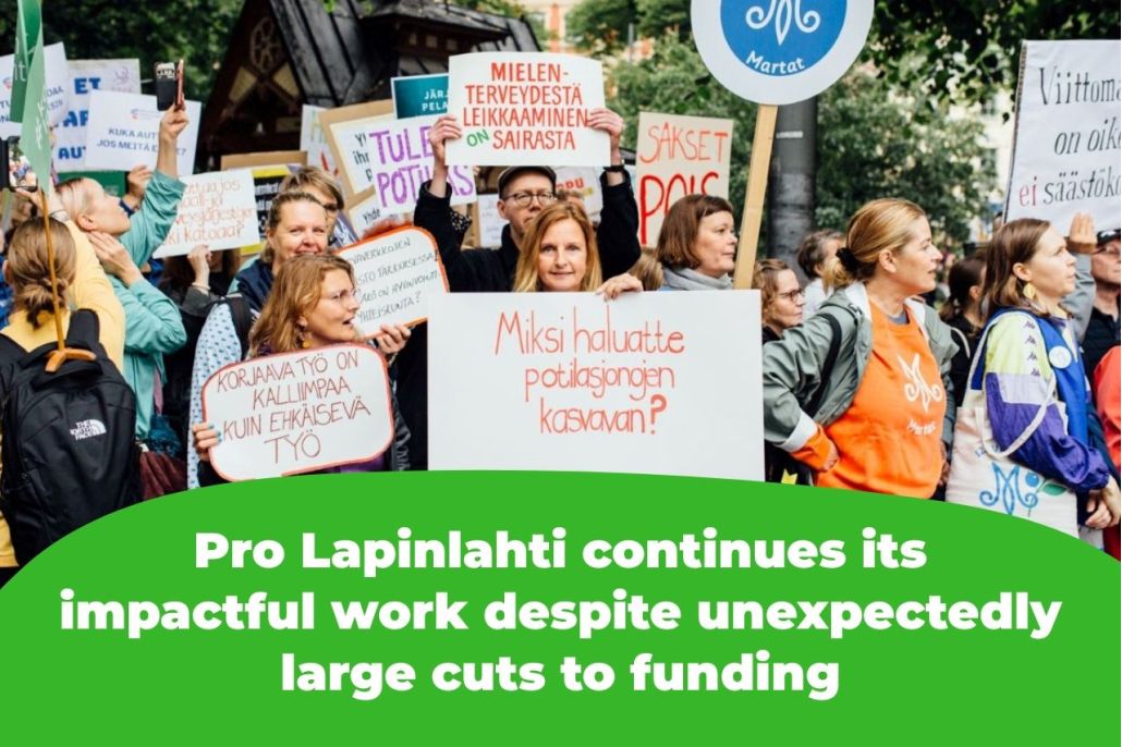 The picture shows protesters holding signs that read, among other things, "Why do you want patient queues to grow?" and "Corrective work is more expensive than preventive work" and "Cutting mental health services is sick."