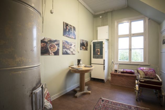 Kuvassa etualalla vasemmalla on takka ja taaempana oikealla pöytä ja jääkaappi.