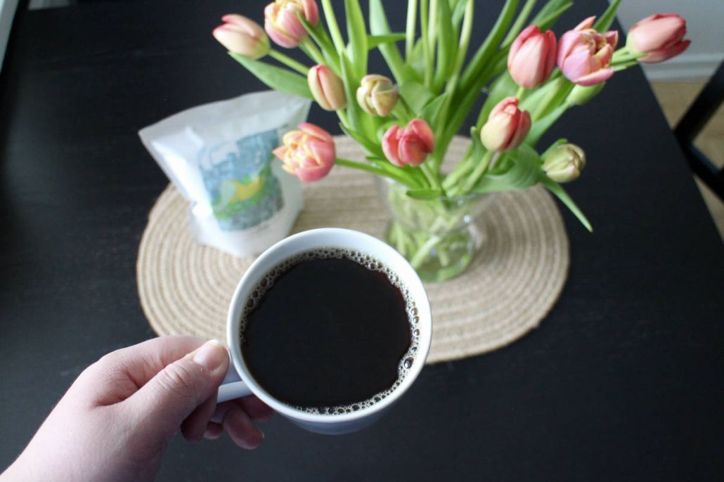 Kuvassa on etualalla kahvikuppi ja takana Save Lapinlahti -kahvipaketti ja tulppaaneja.