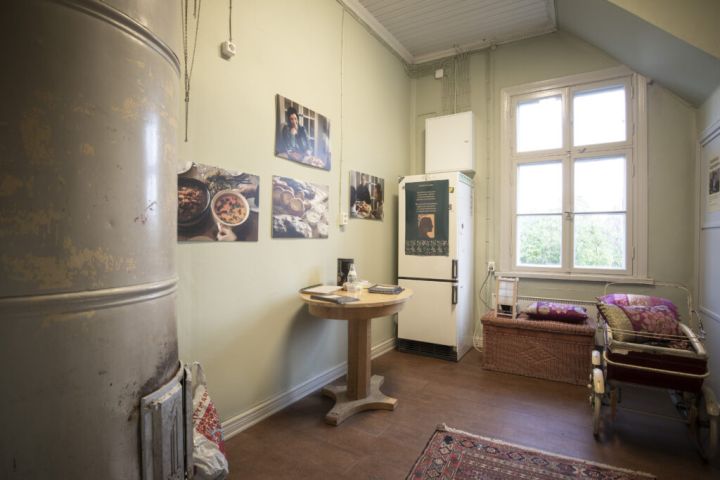 Kuvassa etualalla vasemmalla on takka ja taaempana oikealla pöytä ja jääkaappi.