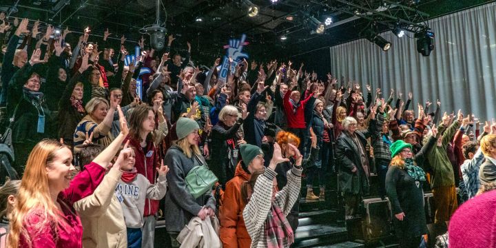 Kuvassa iso sali yleisöä kädet ilmassa kirjasto Oodin salissa.