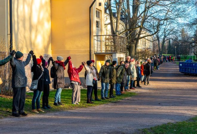 Vuoden 2018 Muuri-tapahtumassa päärakennuksen seinän edessä seisoo ihmisiä käsi kädessä silmänkantamattomiin.